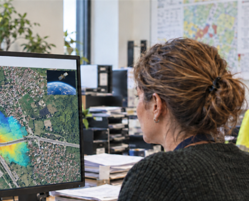 Two infrastructure managers examine an illustrative ground deformation map on a monitor, with a small satellite image in the corner.